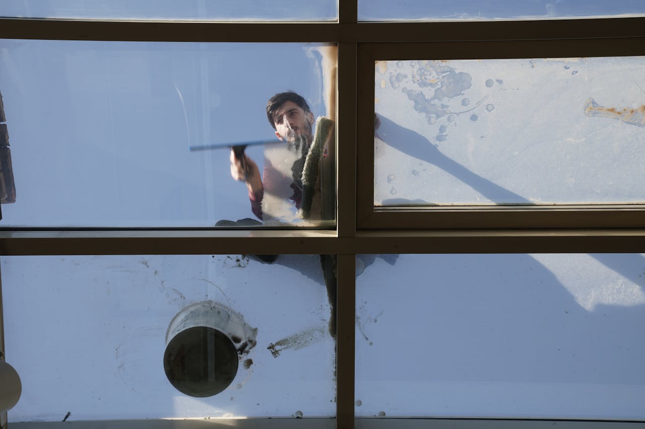 about-01 A male window cleaner washing the exterior glass roof from above with a tool during daylight.